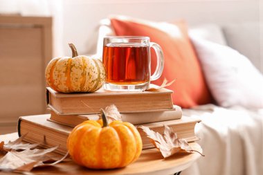 Oturma odasındaki masada balkabaklı, kitaplı ve sonbahar yapraklı bir bardak sıcak çay.