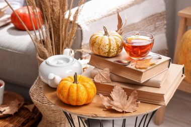 Bir fincan sıcak içecek, balkabağı, kitap ve sonbahar yapraklı bir çaydanlık.