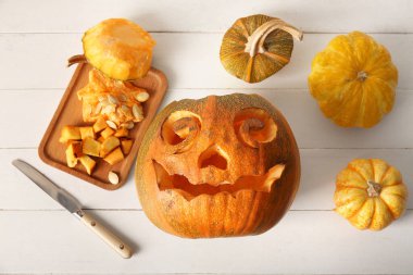 Beyaz ahşap arka planda bıçak ve tahtayla oyulmuş Cadılar Bayramı balkabakları