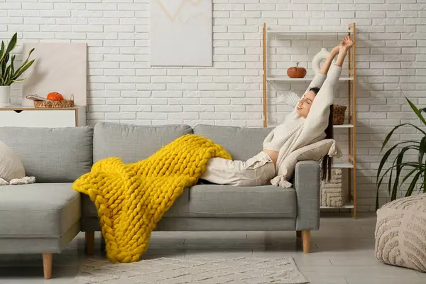 Ilık sarı ekoseli güzel bir kadın kendini uzatıyor ve oturma odasında kanepede uzanıyor.
