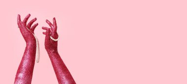 Pembe arka planda inci mücevher tutan parıltılı ellerle kaplı kadın elleri.