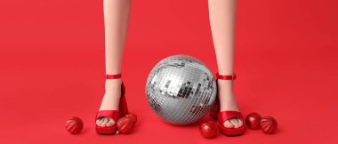 Yüksek topuklu kadın bacakları, Noel mücevherleri ve kırmızı arka planda disko topu. 