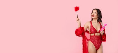Seksi iç çamaşırlı Asyalı kadın, vibratörü ve pembe arka planda tüy çubuğu olan, mesaj için yeri olan.