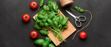 Taze yeşil fesleğenli ahşap tahta ve siyah arka planda domatesler.