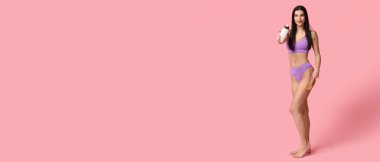 Pembe arka planda fırçası ve bir şişe şampuanı olan genç ve güzel bir kadın.