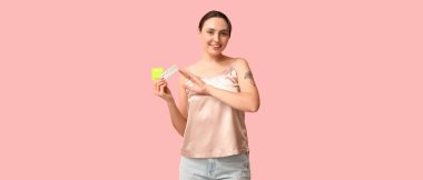 Pembe arka planda prezervatif ve doğum kontrol hapları olan genç bir kadın.
