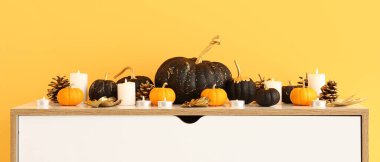 Sarı duvarın yanında balkabaklı çekmeceler ve mumlar.