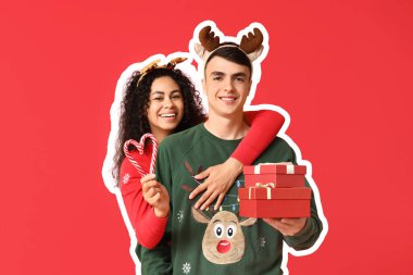 Mutlu genç çift Noel süveteri içinde, hediye kutuları ve kırmızı arka planda şeker kamışlarıyla