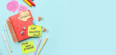 Üzerinde planlar, not defteri ve metin için boşluk olan açık mavi arkaplan üzerine yapışkan notlar. Yeni yıl hedefleri kavramı