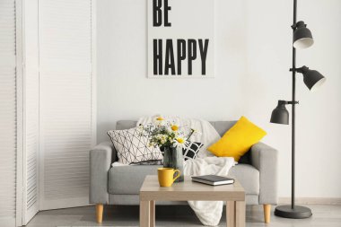 Ahşap masada çiçek açan papatya çiçekleri olan şık bir oturma odası ve vazo.