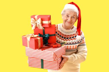 Sarı arka planda Noel Baba şapkalı yaşlı kadın.