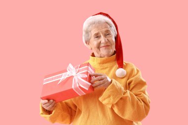 Noel Baba şapkalı yaşlı kadın pembe arka planda Noel hediyesi ile