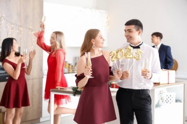 Young couple with champagne and figure 2024 celebrating Christmas in kitchen clipart