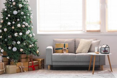 Gri kanepesi ve Noel ağacının altında hediye kutuları olan şenlikli bir oturma odası.