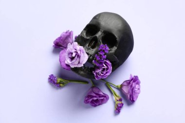 Siyah insan kafatası, mor arka planda güzel çiçekler.