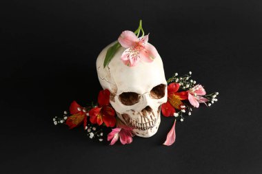 Siyah arka planda güzel zambak ve çigila çiçekleri olan insan kafatası