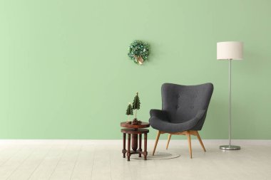 Gri koltuk ve Noel dekoru yeşil duvarın yanındaki ahşap masada.