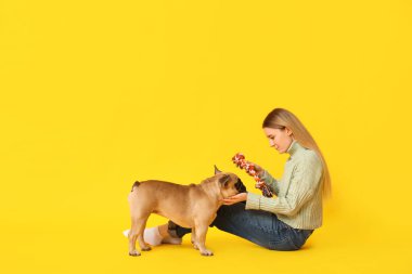 Sarı arka planda sevimli köpekli ve evcil oyuncağı olan güzel genç bir kadın.