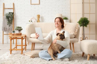 Evde tablet bilgisayar kullanan sevimli köpekli genç bir kadın.