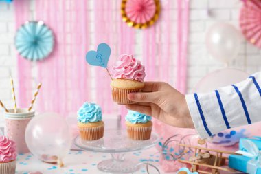 Lezzetli kapkekleri ve dekorasyonları olan beyaz tuğlalı arka planı olan bir kadın. Cinsiyet ortaya çıkan parti kavramı