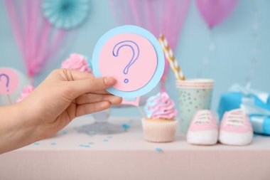 Kağıt soru işareti olan bir kadın el. Kekler ve dekorasyonlar mavi arka planda. Cinsiyet ortaya çıkan parti kavramı