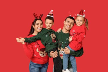 Kırmızı arka planda Noel süveteri giyen mutlu aile