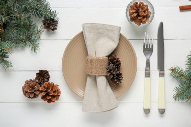 Çam kozalakları ve beyaz ahşap arka planda Noel ağacı dalları olan güzel bir masa.