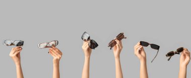 Gri arka planda farklı güneş gözlüklü kadın elleri