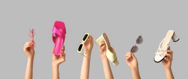 Farklı güneş gözlükleri ve gri arka planda ayakkabıları olan kadın elleri.