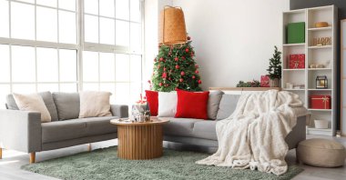 Oturma odasının içinde Noel ağacı ve gri koltuklar var.