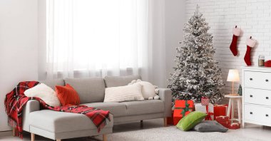 Gri kanepe, Noel ağacı ve hediyelerle aydınlık oturma odasının içinde.