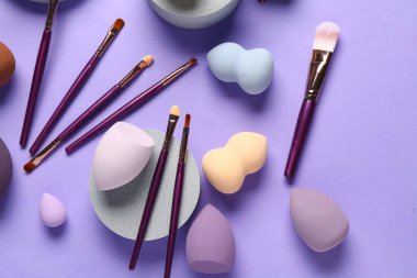 Eflatun arkaplanda makyaj fırçaları ve süngerleri olan dekoratif podyum