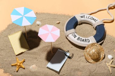 Mini şemsiyeli yaratıcı yaz kompozisyonu, plaj aksesuarları ve bej arka planda kum.