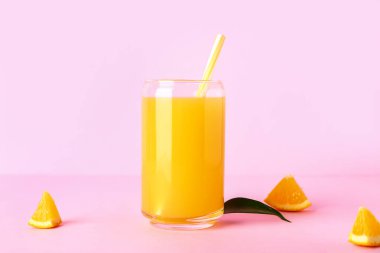 Bir bardak taze portakal suyu ve pembe arka planda yaprak.