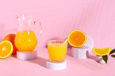 Cam ve pembe arka planda taze portakal suyuyla dekoratif podyumlar