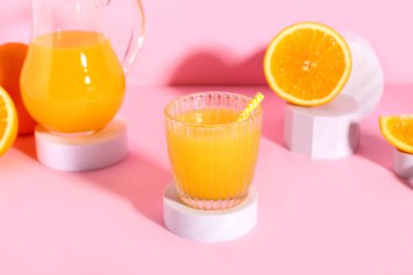 Cam ve pembe arka planda taze portakal suyuyla dekoratif podyumlar