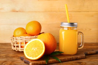 Mason kavanozu taze portakal suyu ve ahşap arka planda meyveler.