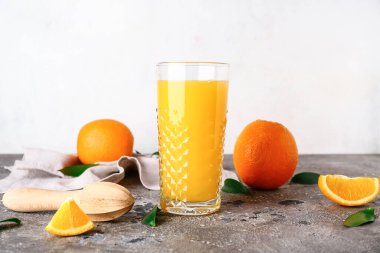 Bir bardak taze portakal suyu, ahşap sıkacağı ve gri masada yapraklar.