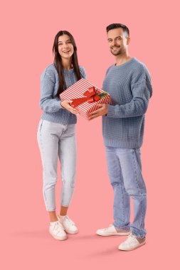 Pembe arka planda Noel hediyesi olan genç bir çift.