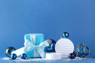 Dekoratif stantlar farklı Noel topları, hediye kutusu ve mavi arka planda kar