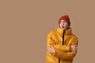 Sıcak kış kıyafetleri içinde güzel genç bir kadın kahverengi arka planda öpücük yolluyor.