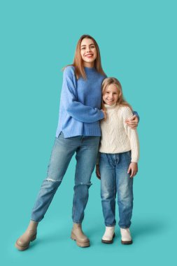 Cute little girl and her mother in winter clothes on blue background clipart