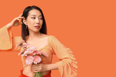 Turuncu arka planda pembe Gerbera çiçekleri olan güzel bir Asyalı kadın.