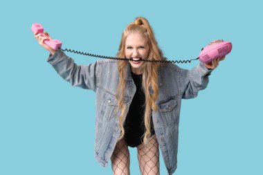 Mavi arka planda retro telefonu olan güzel, kızgın genç bir kadın.