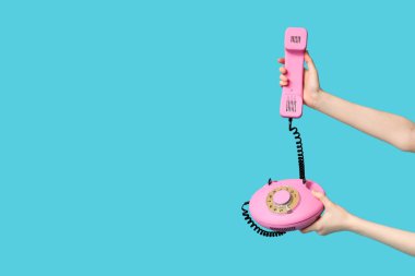 Mavi arka planda retro telefonu olan kadın eller