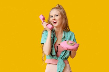 Sarı arka planda retro telefonu olan güzel, genç ve mutlu bir kadın.