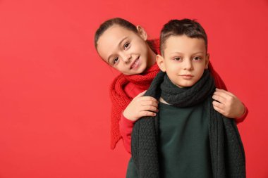 Kırmızı arka planda sıcak kış giysileri içinde şirin küçük mutlu çocuklar.