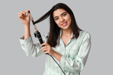 Gri arka planda saç maşası olan güzel bir genç kadın.