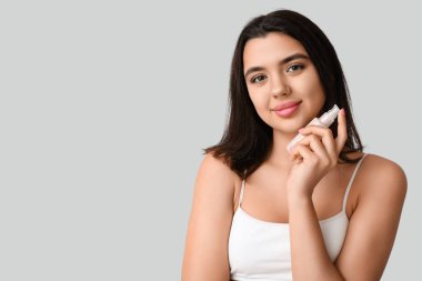 Gri arka planda kozmetik ürünü şişesi tutan güzel genç bir kadın.