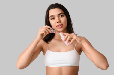 Gri arka planda kozmetik ürünü şişesi tutan güzel genç bir kadın.